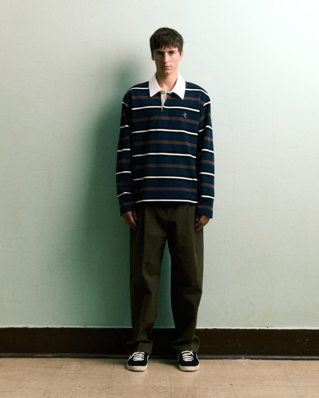 Model wearing LE PÈRE brown multi stripe long-sleeve rugby polo with minimalist styling.